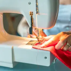 Kobieta szyje na maszynie czerwony materiał, przygotowując się do tego, jak uszyć komin dla dziecka.