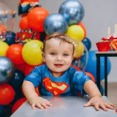 Uśmiechnięty chłopiec w stroju Supermana, otoczony balonami. To dziecko ma w sobie mnóstwo radości i odwagi, co są jego mocne strony, przykłady widać w jego spojrzeniu.