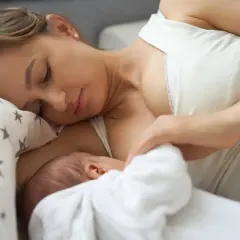 Delikatny uścisk matki, karmiącej dziecko. Mleko matki ma naturalny, białawy kolor, symbolizujący czystość i odżywienie.