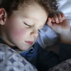 Mały chłopiec śpi pod kołdrą. Może nawet mówi przez sen, opowiadając o swoich snach.