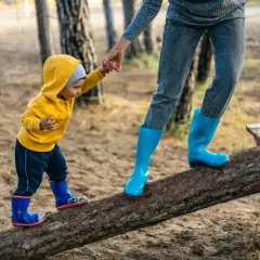 Dziecko w żółtej bluzie i mama w niebieskich kaloszach idą po kłodzie. Czy po szczepieniu można iść z dzieckiem na spacer? Tak, jeśli czuje się dobrze!
