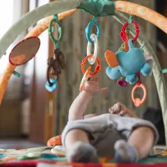 Niemowlę sięga do kolorowych zabawek sensorycznych dla niemowlaka wiszących na macie edukacyjnej.