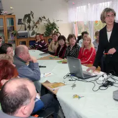 Nauczyciele zebrani na radzie pedagogicznej, dyskutują przy stole z laptopem i projektorem.