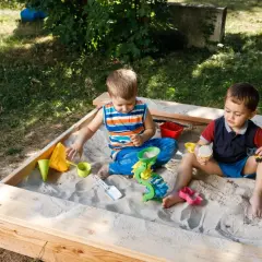 Dwóch chłopców bawi się w piaskownicy, budując zamki z piasku. To świetny sposób, jak zrobić piaskownicę i zapewnić dzieciom rozrywkę.