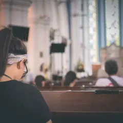 Kobieta w kościele, być może jako patron na bierzmowanie, siedzi w ławce. W tle widać ołtarz i witraże.