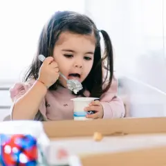 Mała dziewczynka z kitkami zajada łyżeczką pyszne danonki dla dzieci.