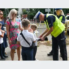 Policjant pomaga dziecku przejść przez ulicę, przypominając, od ilu lat dziecko może samo chodzić do szkoły.