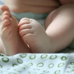 Małe, pulchne nóżki niemowlaka, lekko spocone stopy u niemowlaka, odpoczywają na miękkiej, wzorzystej tkaninie.