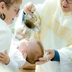 Chrzest dziecka w kościele. Kapłan polewa głowę niemowlęcia wodą święconą.
