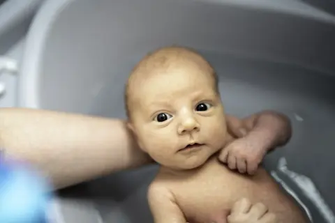 Niemowlę w wanience, z zaciekawieniem patrzy na świat. Czy można kąpać dziecko po szczepieniu? Tak, jeśli nie ma przeciwwskazań lekarza.