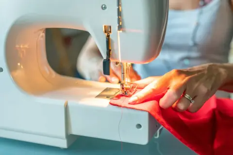 Kobieta szyje na maszynie czerwony materiał, przygotowując się do tego, jak uszyć komin dla dziecka.