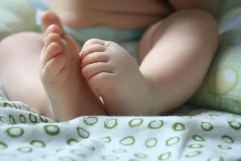 Małe, pulchne nóżki niemowlaka, lekko spocone stopy u niemowlaka, odpoczywają na miękkiej, wzorzystej tkaninie.