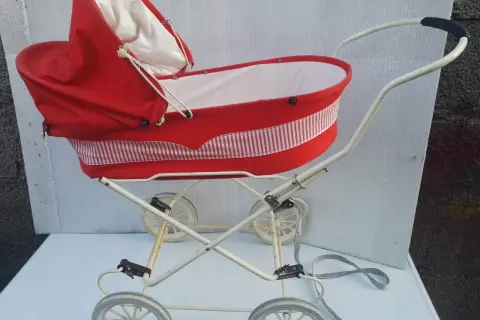 Czerwony wózek dziecięcy z białymi paskami, stylizowany na lata 60., z kremową wyściółką i metalowym stelażem.