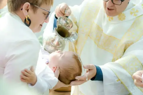 Chrzest dziecka w kościele. Kapłan polewa głowę niemowlęcia wodą święconą.