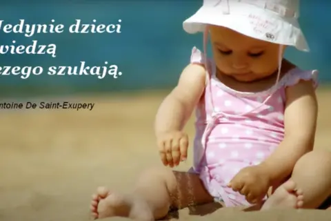 Dziecko na plaży, w różowym stroju w kropki, bawi się piaskiem. Cytat: "Jedynie dzieci wiedzą czego szukają.