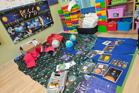 Materiały do stworzenia stroju kosmicznego dla dziecka: plakaty z planetami, globusy, srebrna maska, czerwone ubranie.