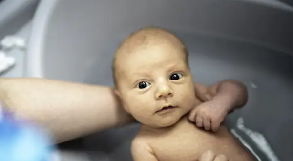Niemowlę w wanience, z zaciekawieniem patrzy na świat. Czy można kąpać dziecko po szczepieniu? Tak, jeśli nie ma przeciwwskazań lekarza.