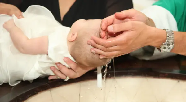 Chrzest dziecka. Matka chrzestna z rodziną wspiera maluszka podczas obrzędu.