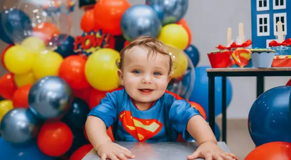 Uśmiechnięty chłopiec w stroju Supermana, otoczony balonami. To dziecko ma w sobie mnóstwo radości i odwagi, co są jego mocne strony, przykłady widać w jego spojrzeniu.