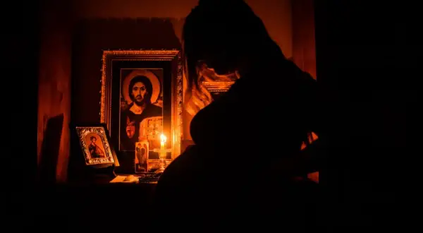 Ciężarna kobieta w mroku klęczy przed ikonami i płonącą świecą. Jej serce przepełnia modlitwa o szczęśliwy poród dla córki.