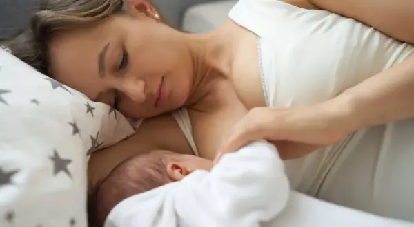 Delikatny uścisk matki, karmiącej dziecko. Mleko matki ma naturalny, białawy kolor, symbolizujący czystość i odżywienie.