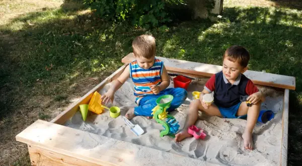 Dwóch chłopców bawi się w piaskownicy, budując zamki z piasku. To świetny sposób, jak zrobić piaskownicę i zapewnić dzieciom rozrywkę.