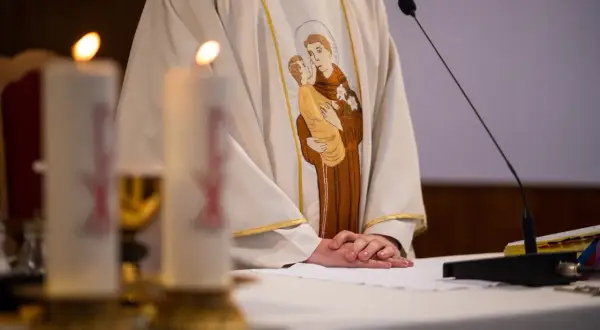 Ksiądz w szacie z haftem przedstawiającym św. Antoniego z Dzieciątkiem Jezus, przy ołtarzu ze świecami.