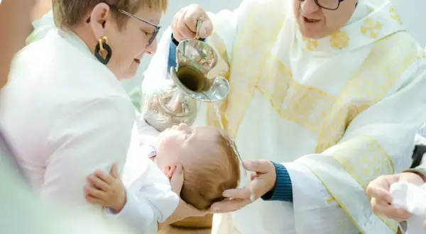 Chrzest dziecka w kościele. Kapłan polewa głowę niemowlęcia wodą święconą.