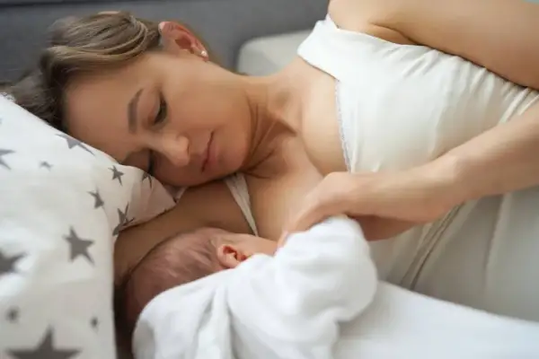 Delikatny uścisk matki, karmiącej dziecko. Mleko matki ma naturalny, białawy kolor, symbolizujący czystość i odżywienie.