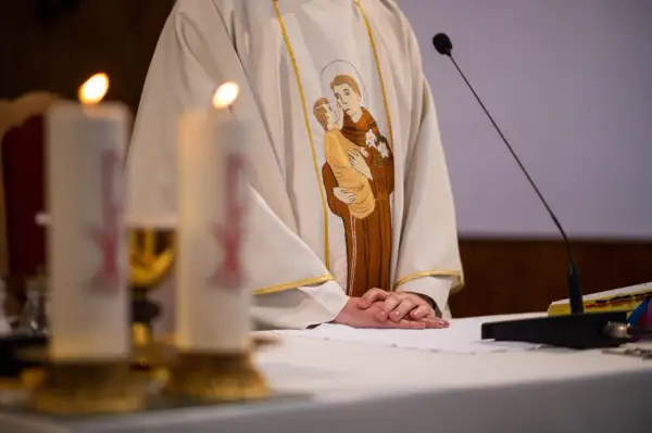 Ksiądz w szacie z haftem przedstawiającym św. Antoniego z Dzieciątkiem Jezus, przy ołtarzu ze świecami.