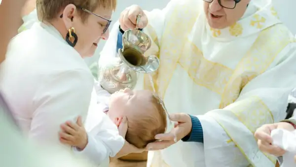 Chrzest dziecka w kościele. Kapłan polewa głowę niemowlęcia wodą święconą.